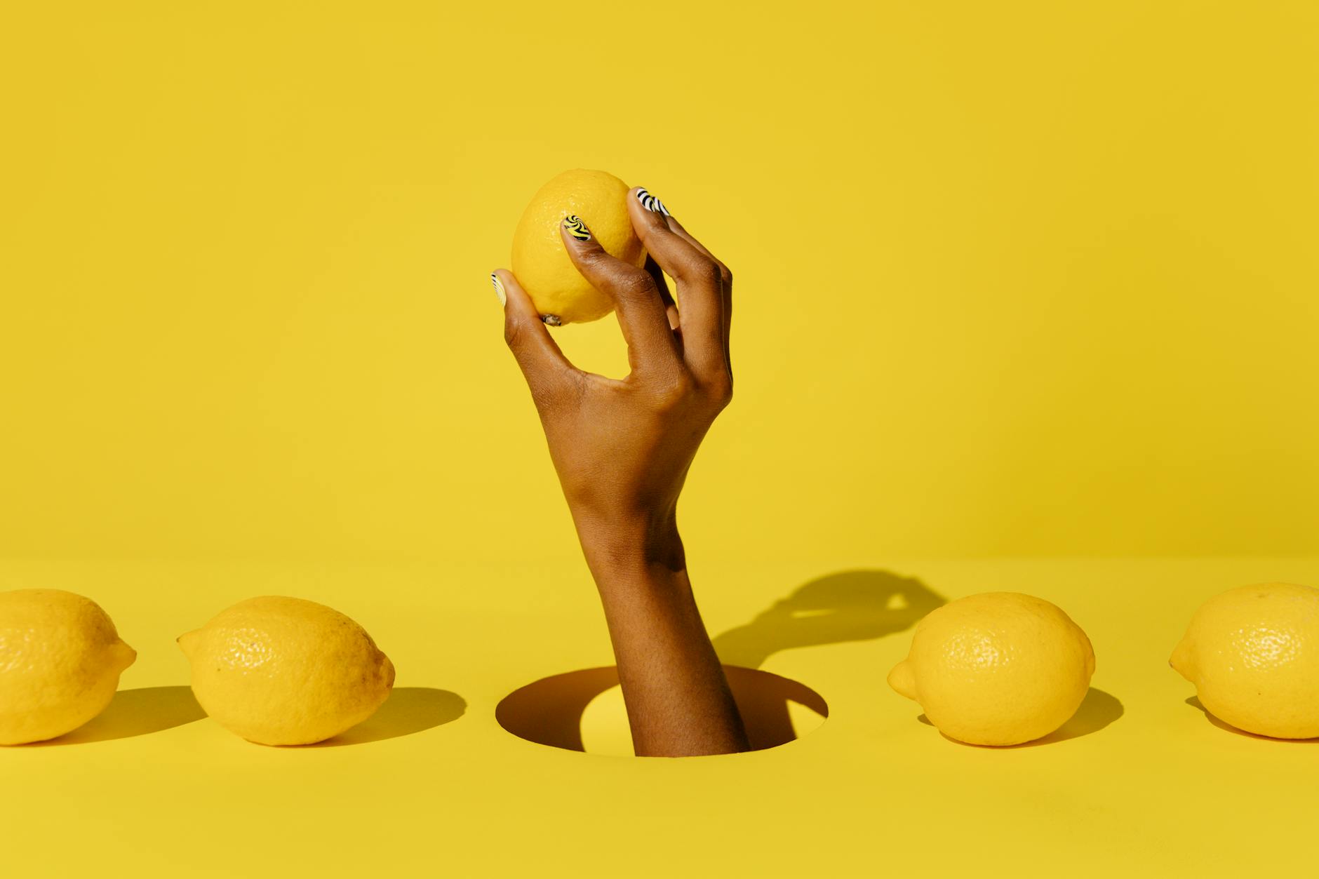 A hand holding a lemon against a yellow background, symbolizing hope and renewal after loss