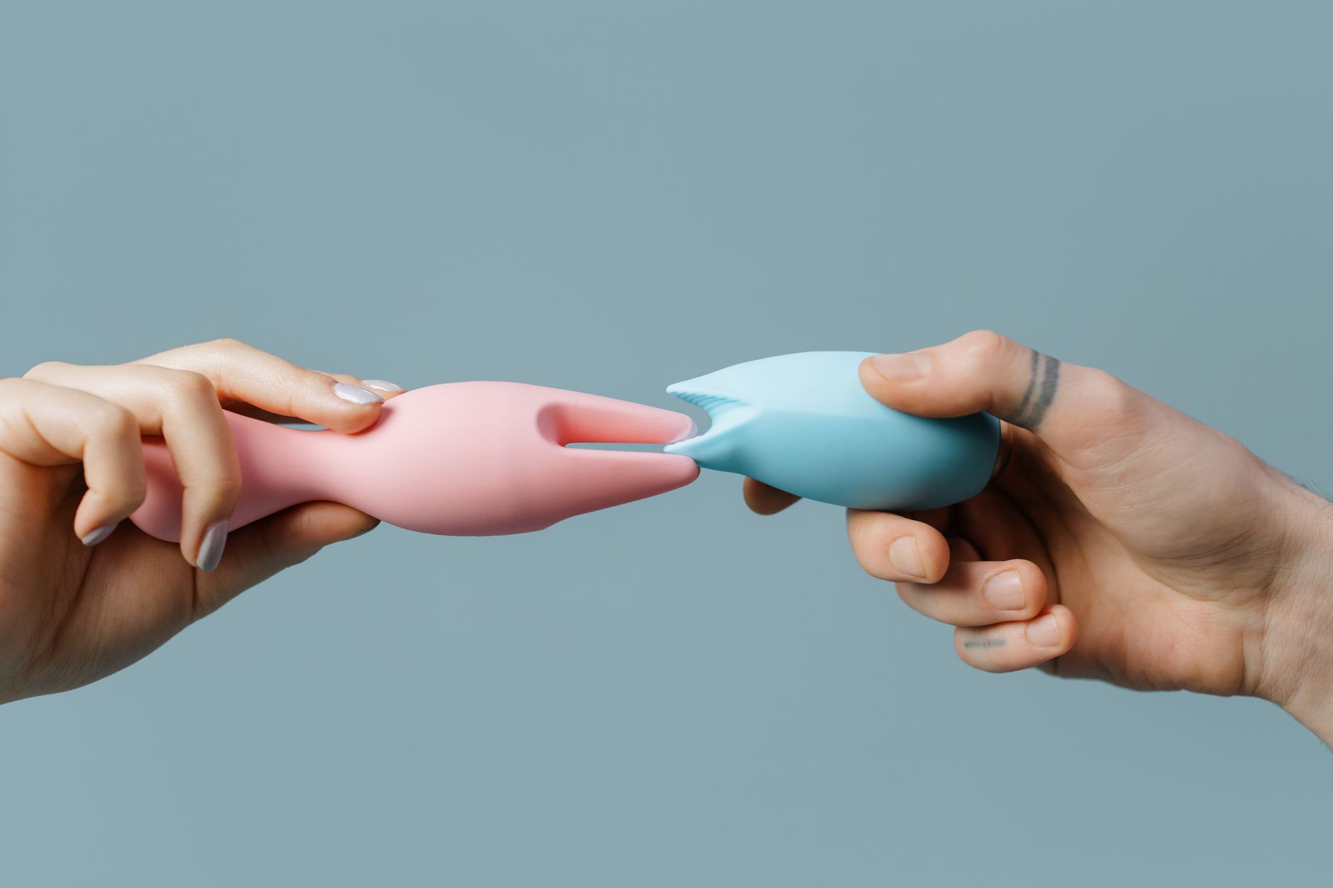 Hands holding pastel-colored silicone lemon vibrators against a soft background