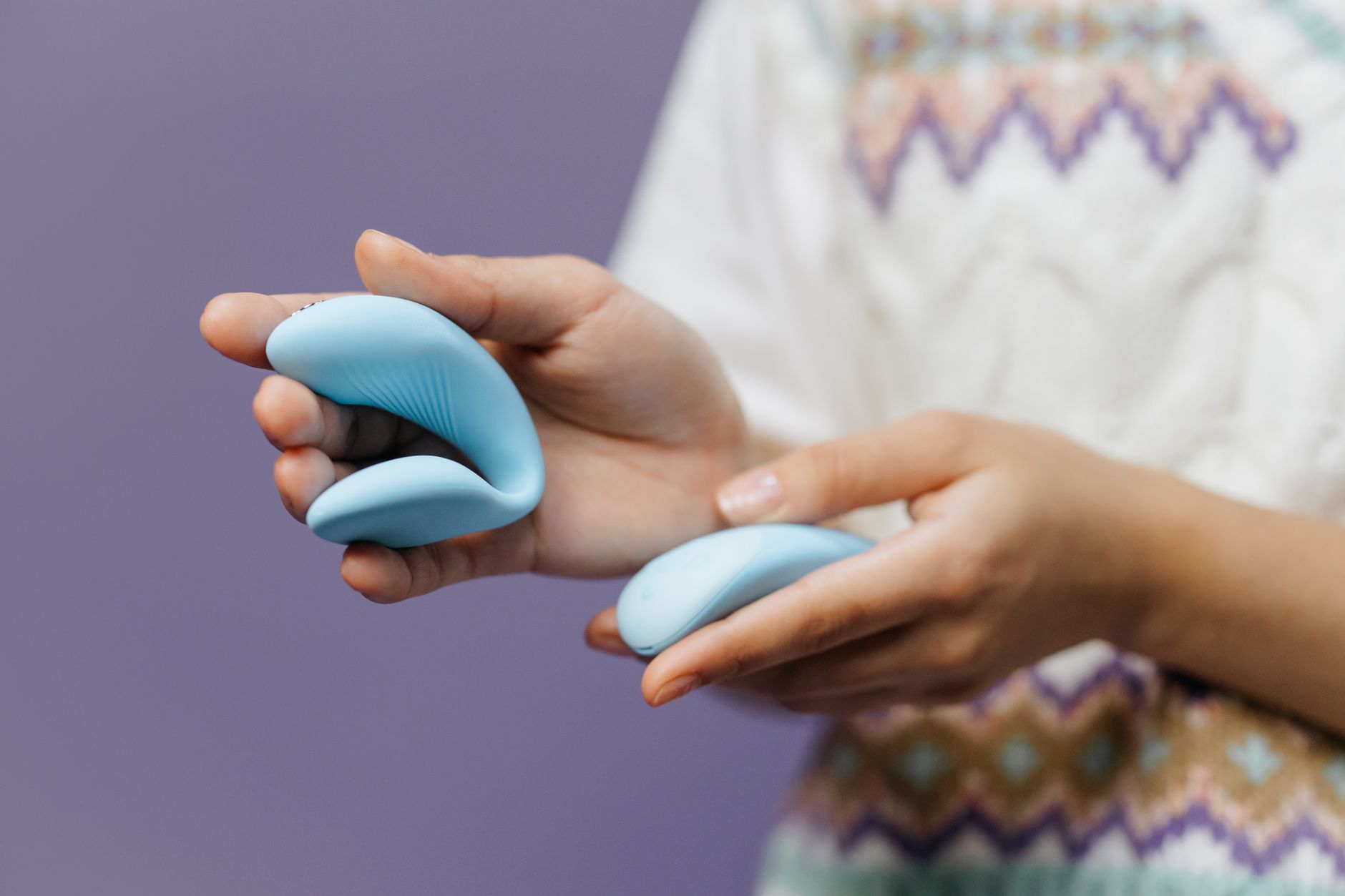 A hand reaching over a variety of colorful silicone vibrators arranged on a table, displaying different shapes and designs.