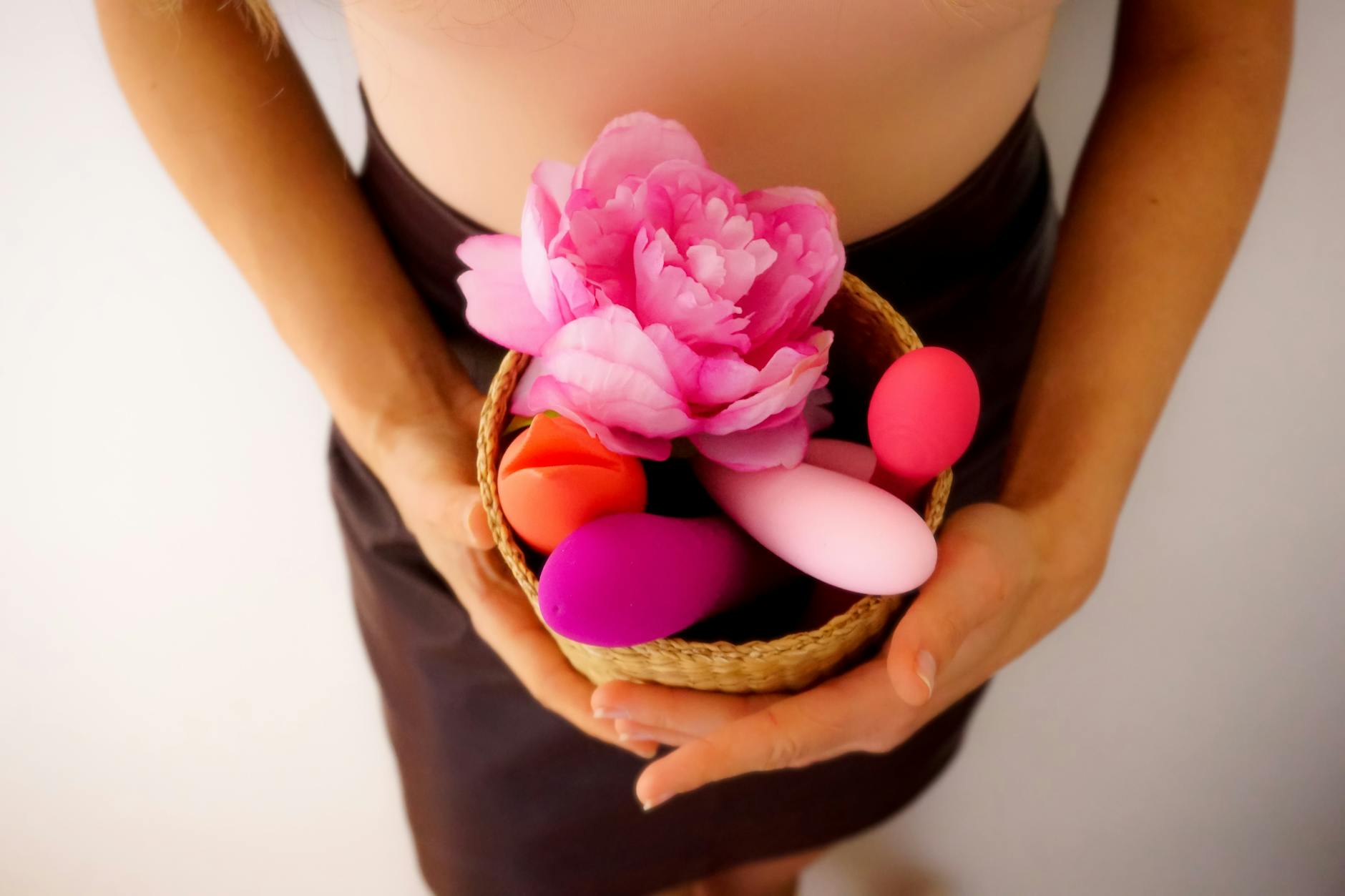 A collection of colorful vibrators in a basket with flowers, representing safe pleasure exploration.